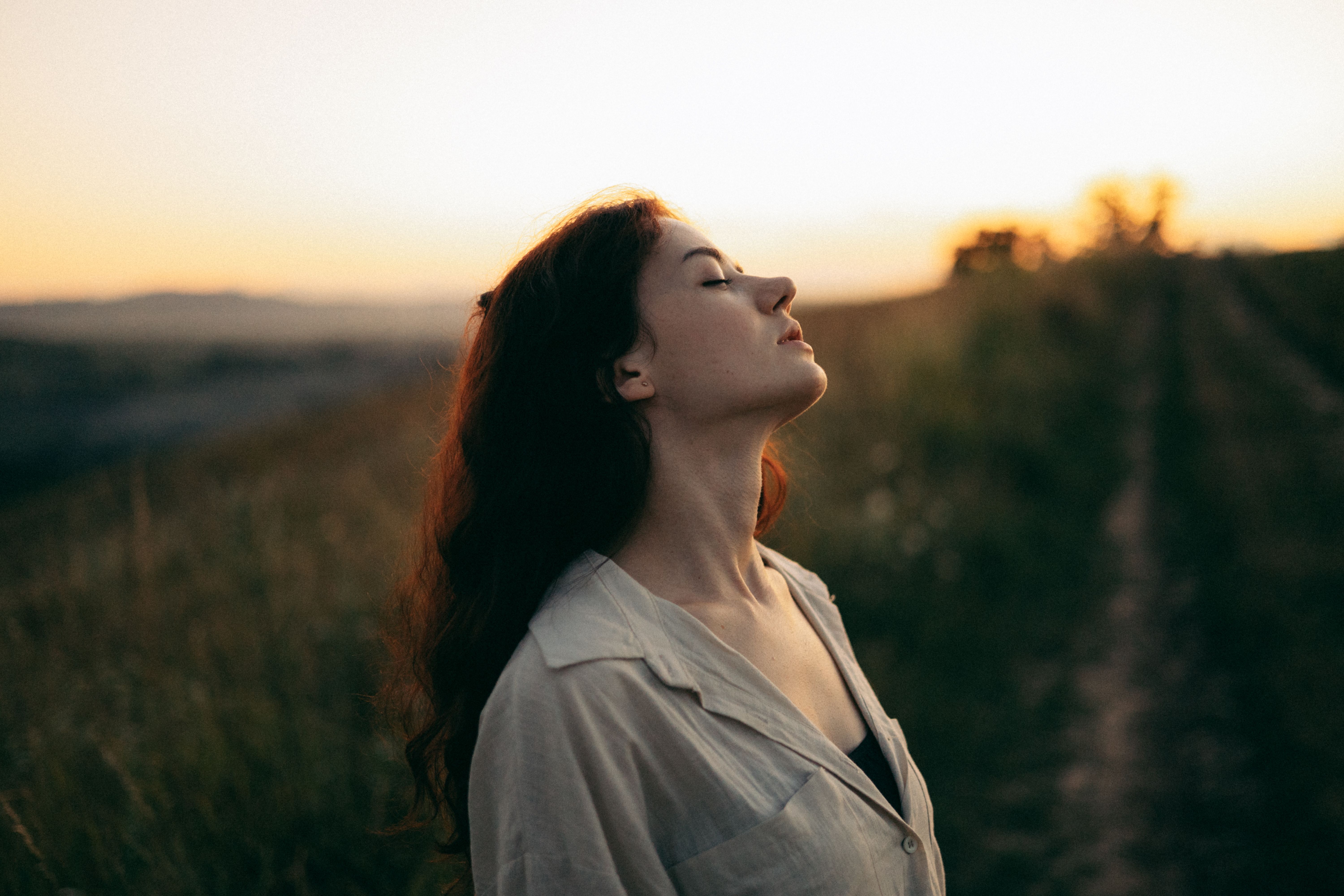 Peaceful person outdoors with eyes closed and a relaxed expression while enjoying a quiet natural environment.