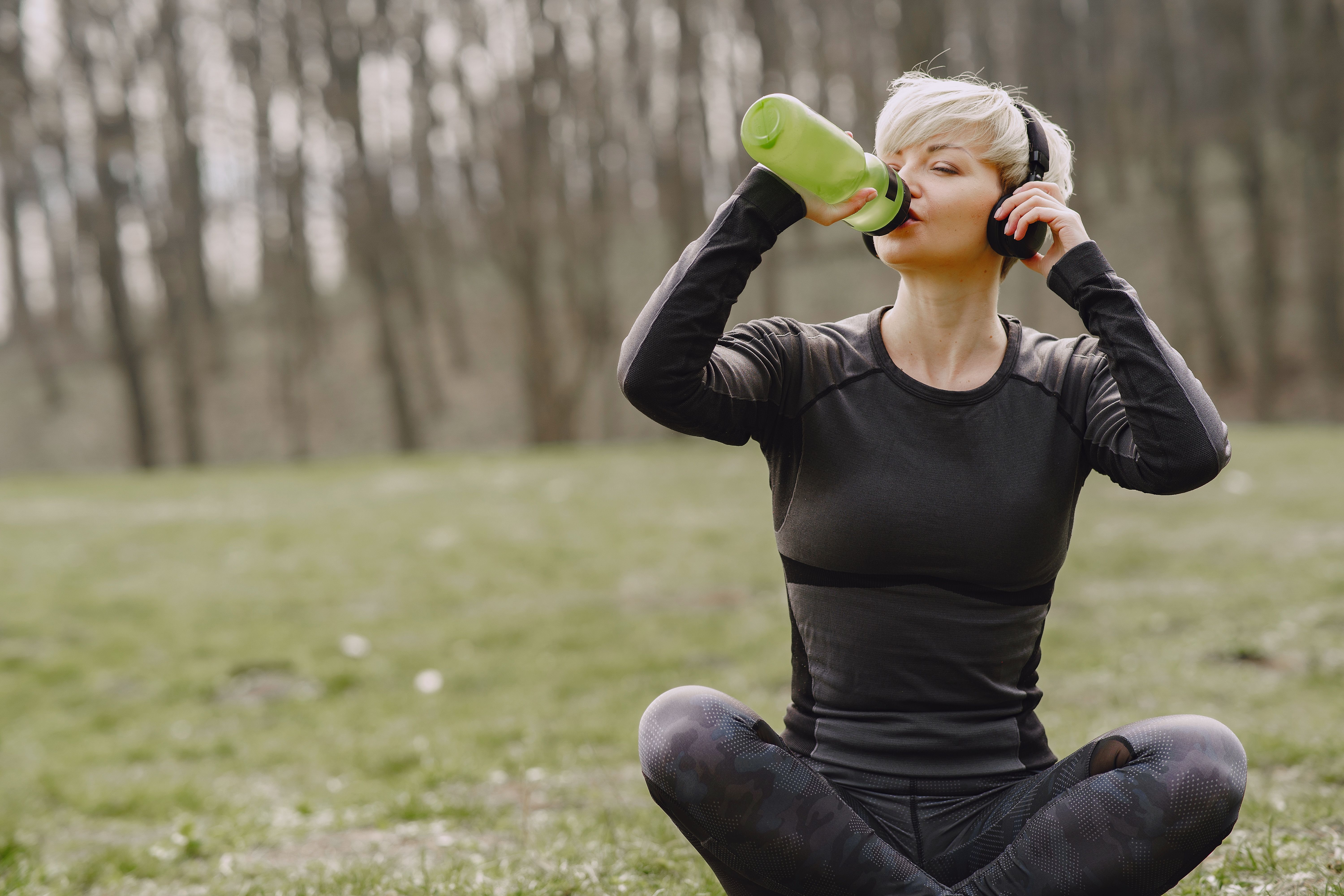 Energetic active person drinking a glass of water outdoors during the afternoon as part of a healthy lifestyle.